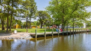 Ein Park am Seeufer mit Picknicktischen, einem Spielplatz und einer Holzsteganlage, die sich ins Wasser erstreckt.