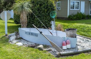 Un bote con un letrero que dice "MOC MD" en un terreno cubierto de césped, con rocas y una casa al fondo.