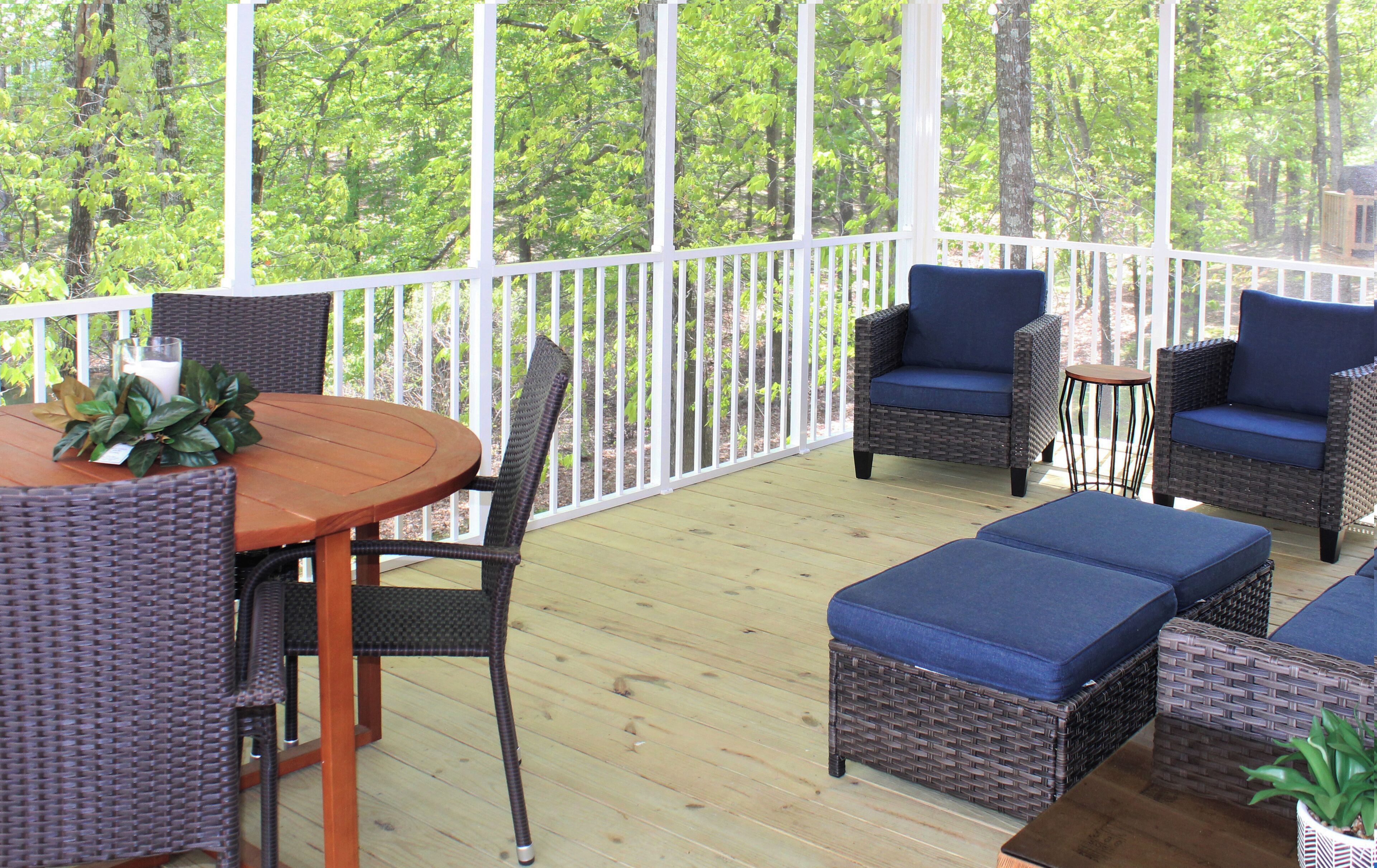 Eine überdachte Terrasse im Freien mit Korbmöbeln, einem Holztisch und Blick auf einen Wald.