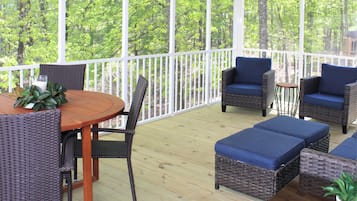 Eine überdachte Terrasse im Freien mit Korbmöbeln, einem Holztisch und Blick auf einen Wald.