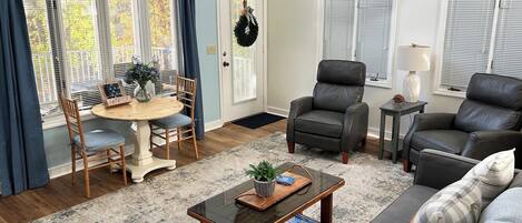 A living room with a round wooden table, two chairs, a sofa, a coffee table, and a fireplace.