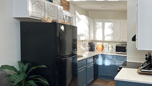 A modern kitchen with a black refrigerator, blue cabinets, a wooden countertop, and a grey sofa.