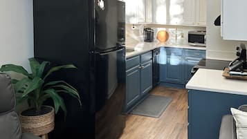 Eine moderne Küche mit einem schwarzen Kühlschrank, blauen Schränken, einer Holzarbeitsplatte und einem grauen Sofa.