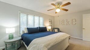 A bedroom with a bed, a ceiling fan, a nightstand, a lamp, and a wall with the word "lake" spelled out. - Two Bedroom Bayside Condo (Grand Rivers)