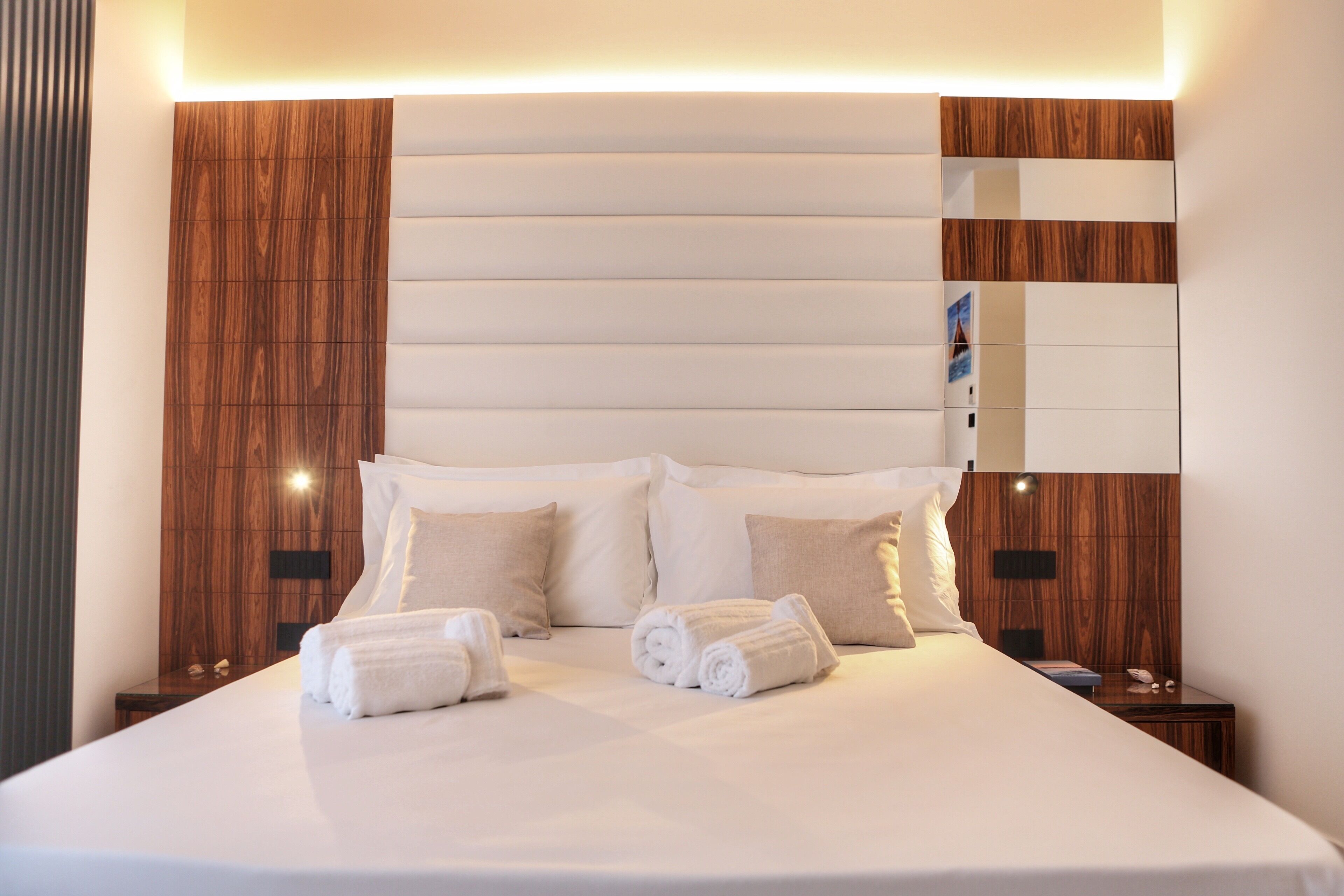 A modern hotel room with a large bed, wooden headboard, and a nightstand with a phone and a lamp.