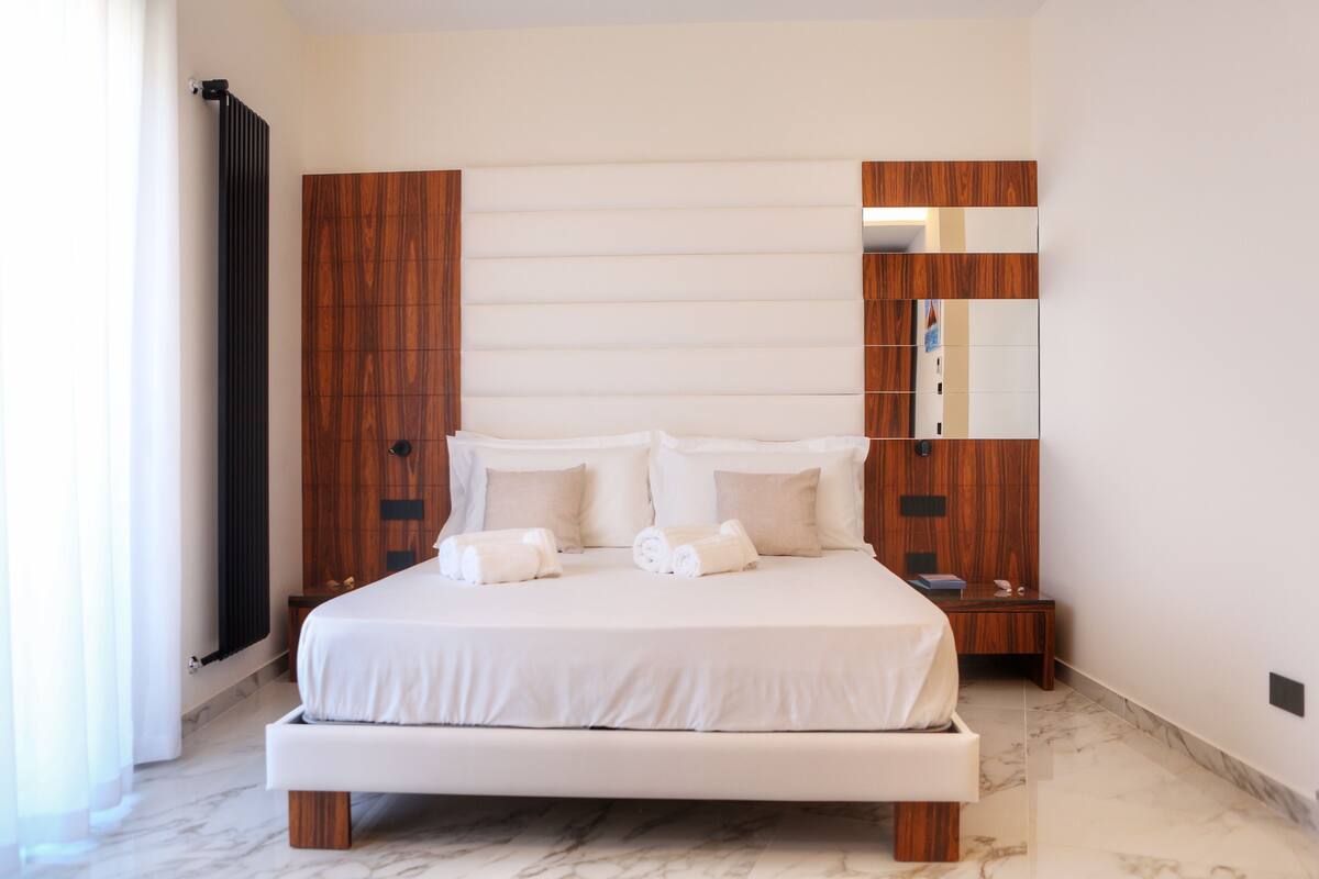 A modern bedroom with a large bed, wooden headboard, and a nightstand.