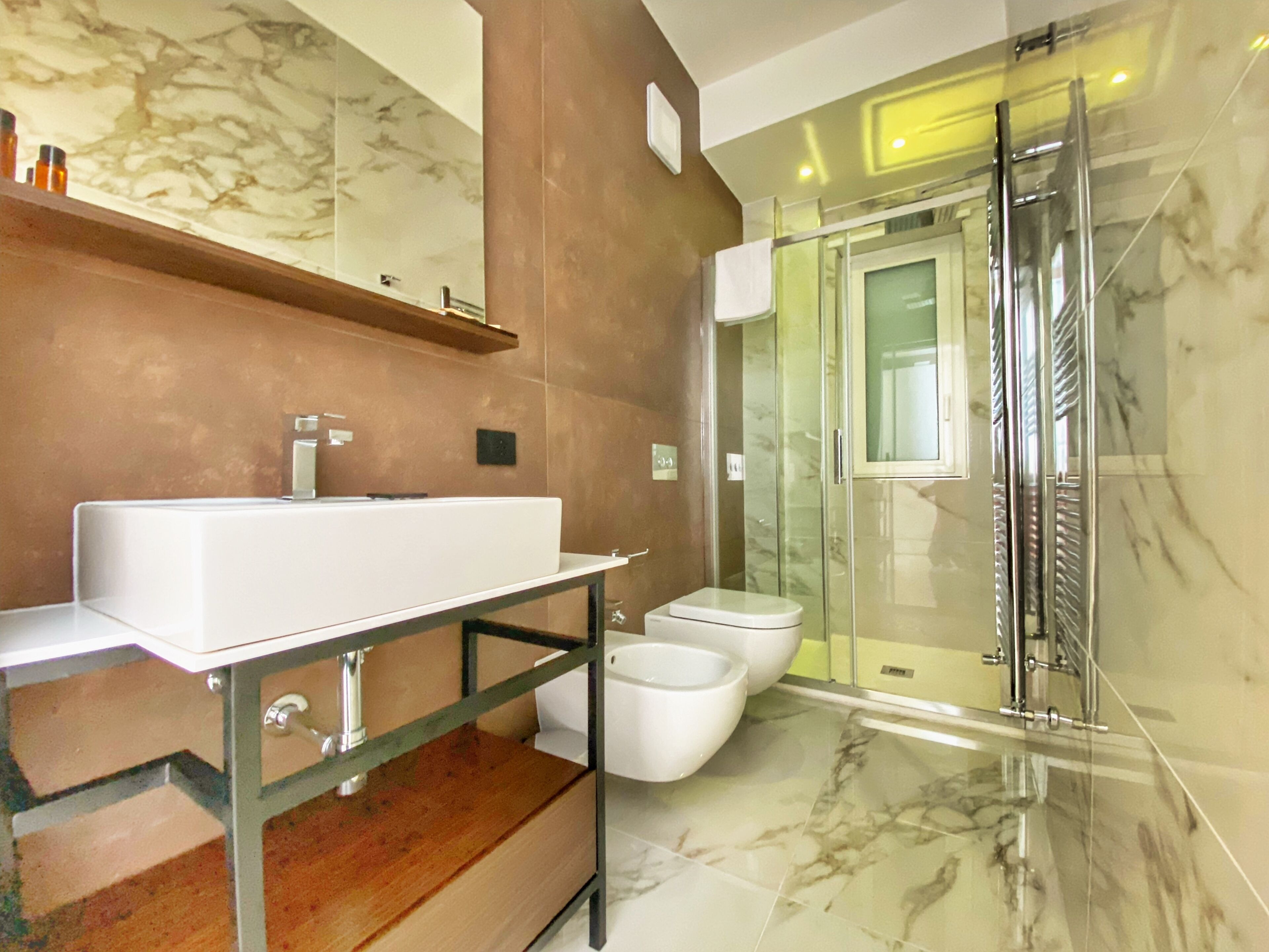 Un bagno moderno con un lavabo in marmo, box doccia in vetro e una scala in legno.