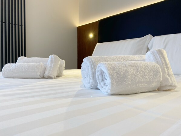 A hotel room with neatly folded white towels on the bed, a modern headboard, and a striped bedspread. - BorgiaRooms (Milazzo)