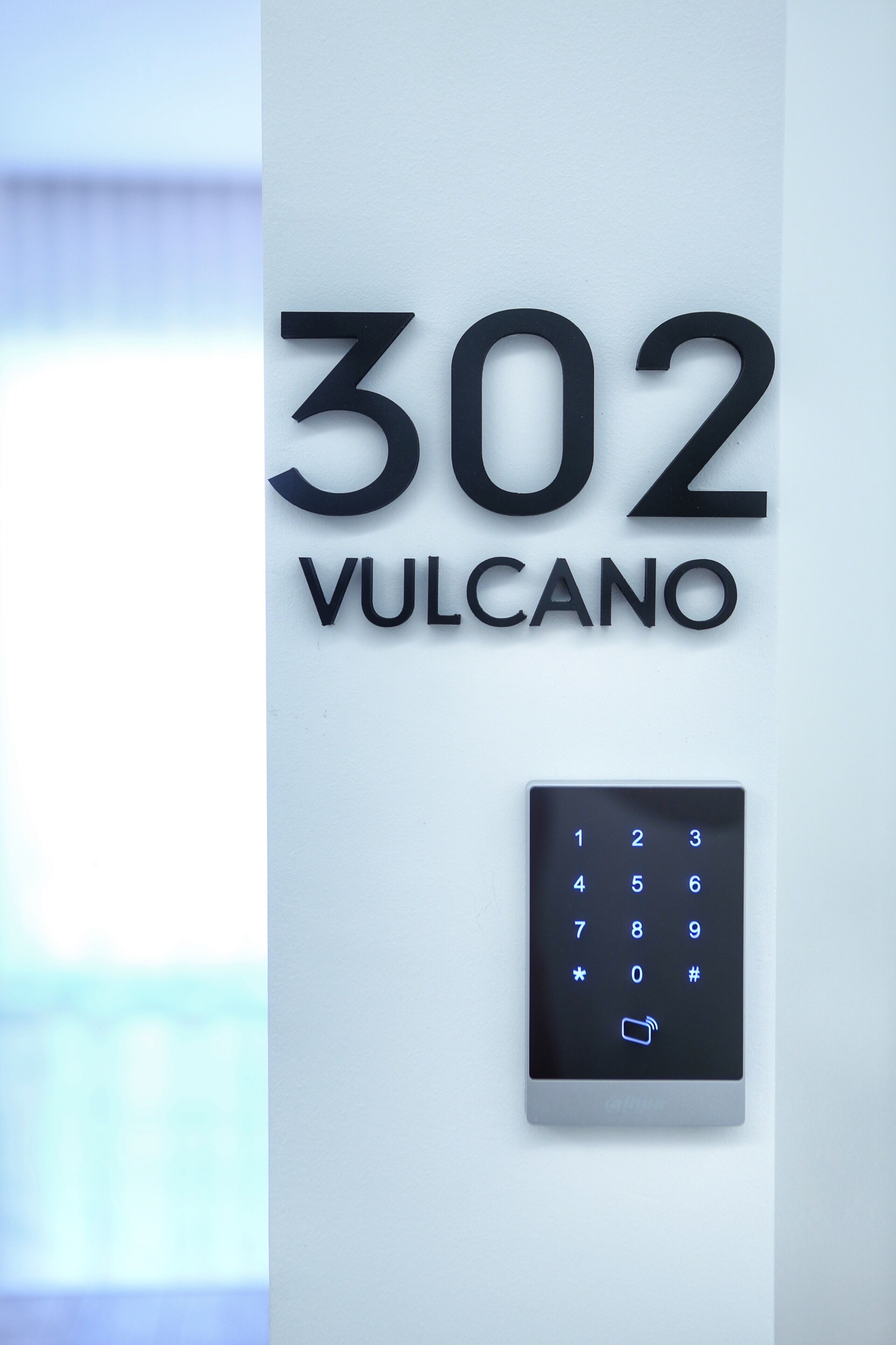 A wall-mounted sign with the number "302" and the word "VULCANO" indicating a hotel room number. Below the sign, there is a keypad for room access.