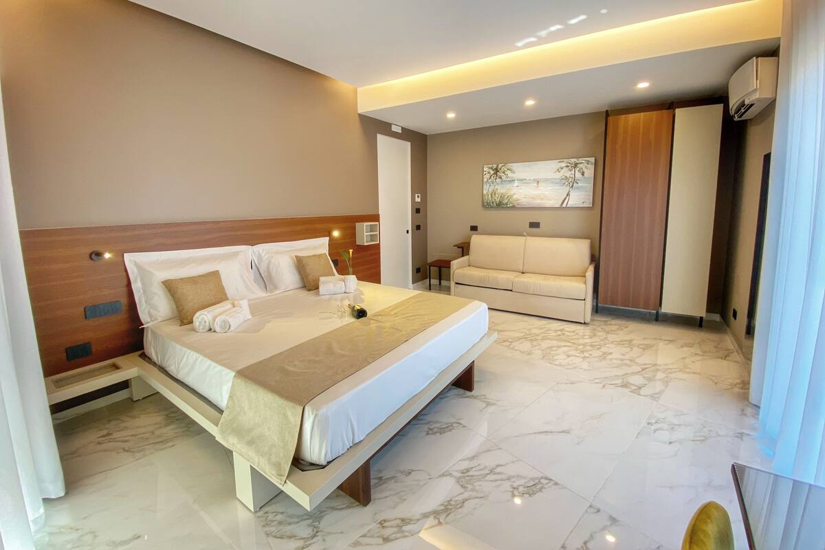 A modern hotel room with a large bed, a sofa, and a painting on the wall.