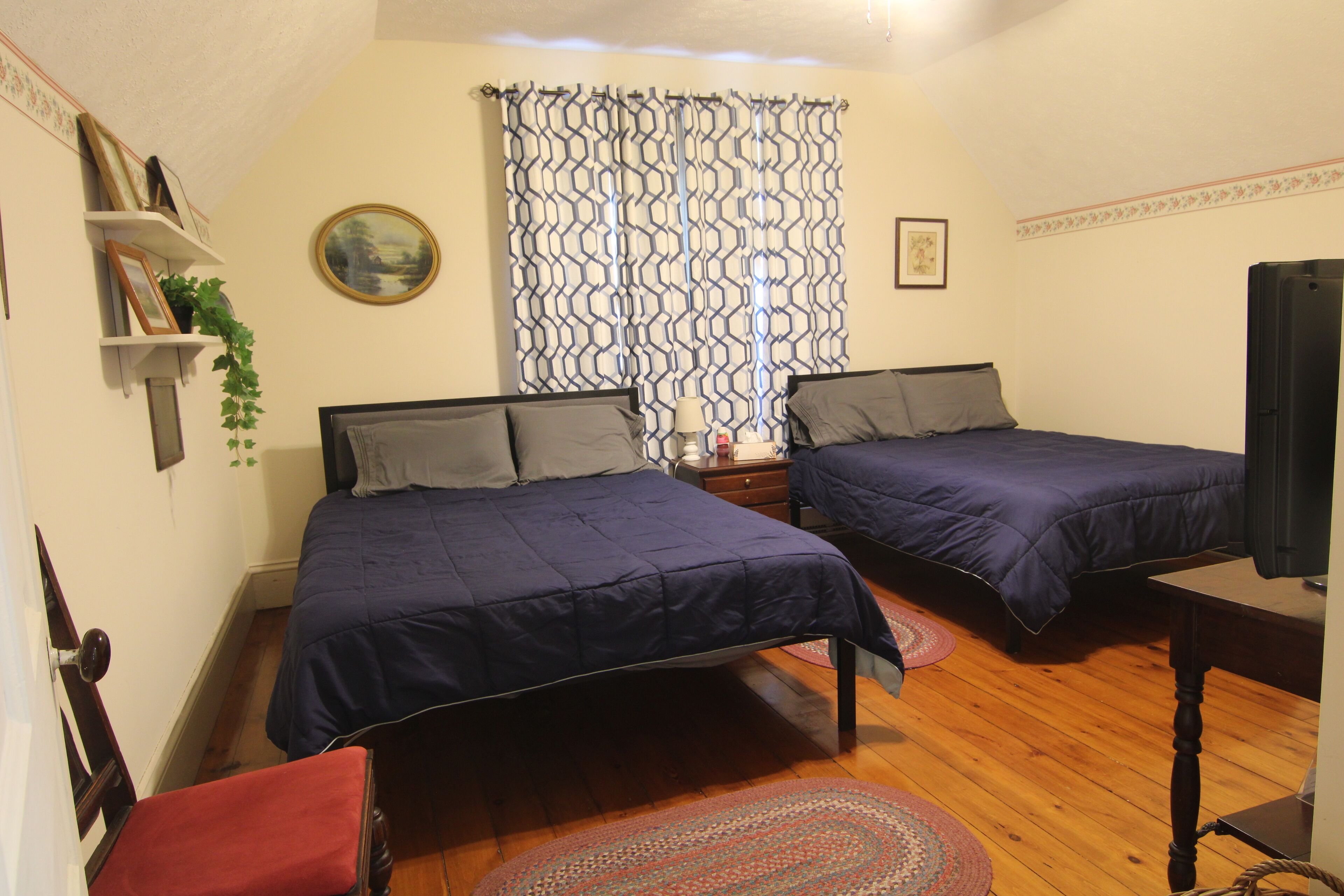 Een slaapkamer met twee bedden, een televisie, een plank met foto's en een raam met patroon gordijnen.