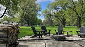 Un patio con sillas Adirondack, un brasero y una pila de leña.