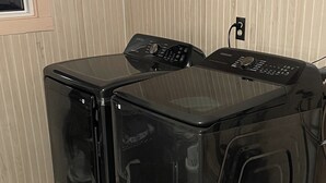 Dos lavadoras frontales negras en una habitación con papel tapiz color beige y piso de baldosas.