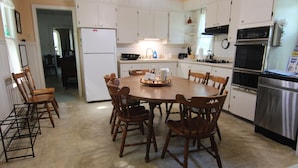 Una cocina con armarios blancos, horno de acero inoxidable y una mesa de comedor con sillas de madera.