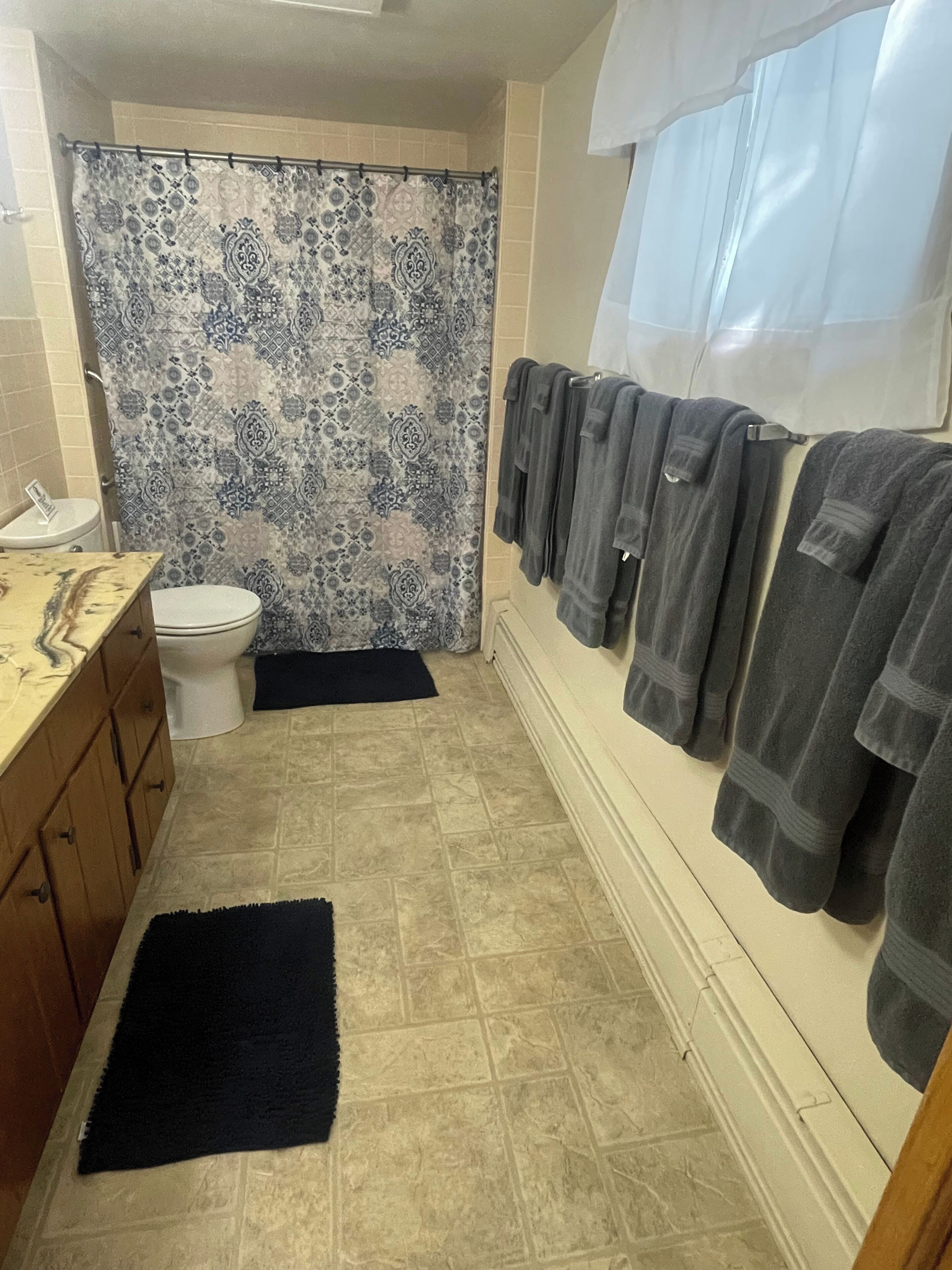 Ein Badezimmer mit gemustertem Duschvorhang, Toilette, Waschbecken mit Spiegel und Handtüchern an einem Wäscheständer.