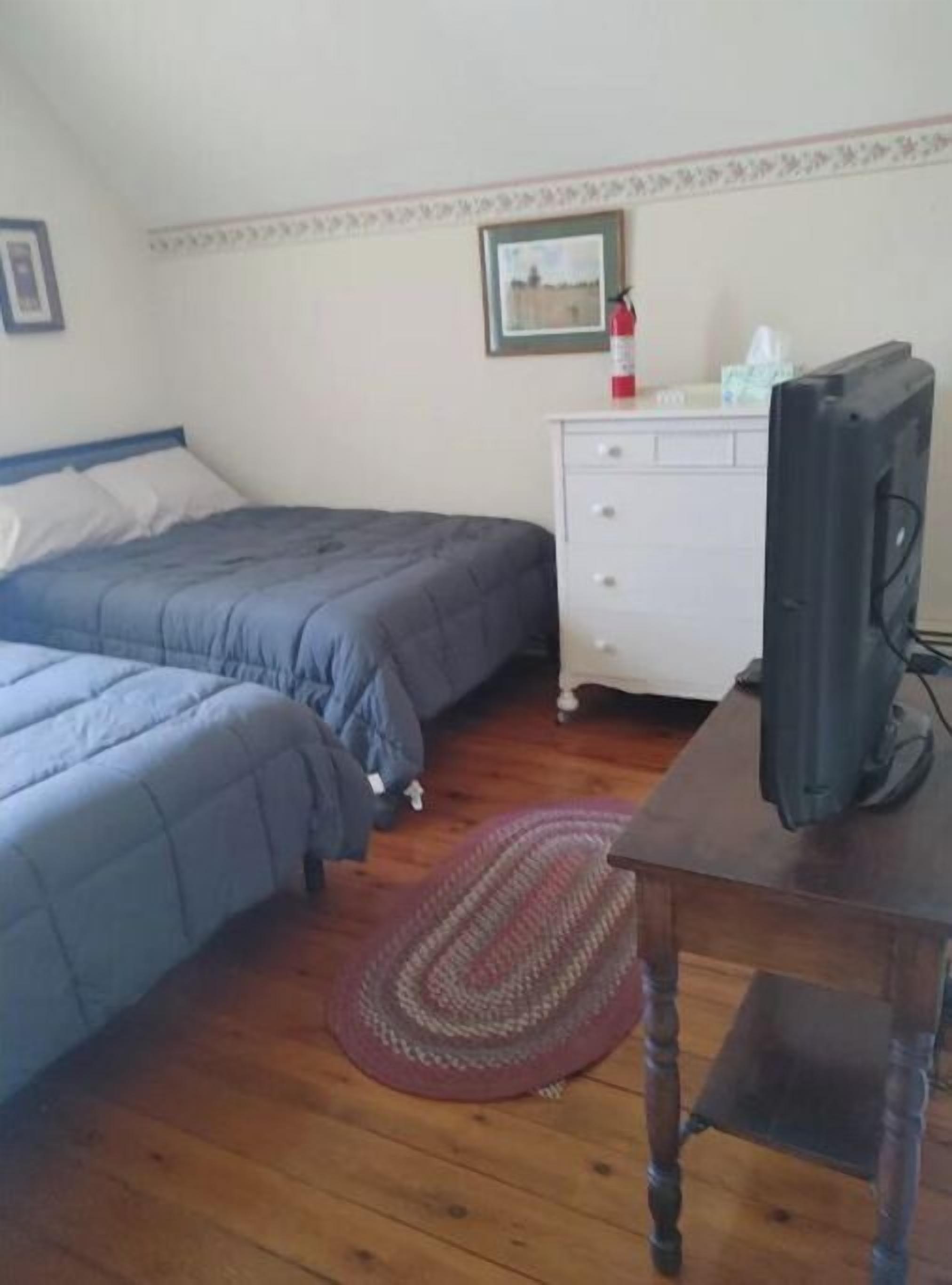 Un dormitorio con dos camas, un aparador, una televisión y un cuadro en la pared.