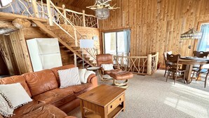 Ein Blockhaus-Interieur mit Ledersofa, Holztisch und einem Essbereich mit Stühlen und Tisch.