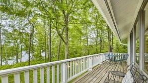 Eine Holzterrasse mit weißer Geländer, Gartenmöbeln und Blick auf einen bewaldeten Bereich.