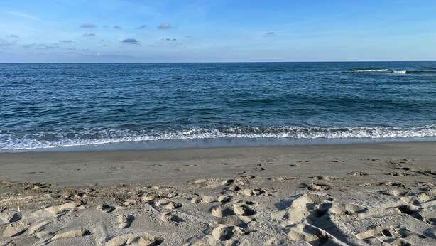 A beach with footprints in the sand and the ocean in the background.