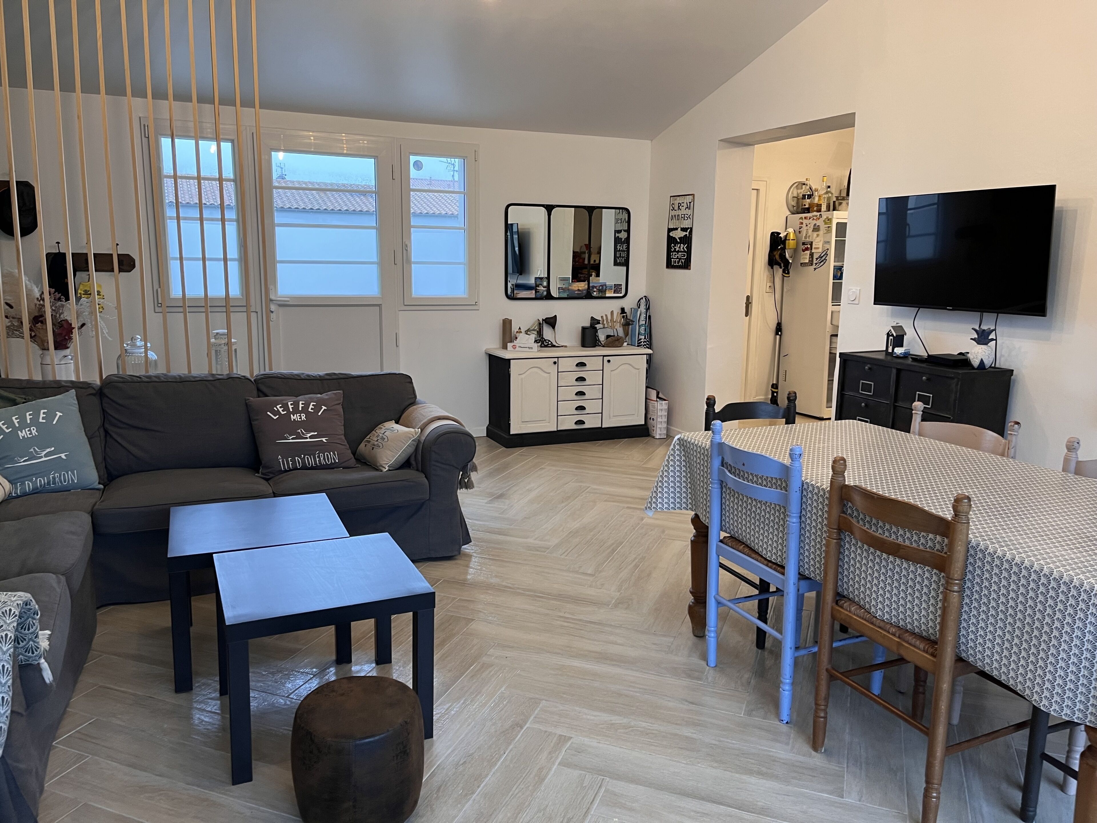 Een woonkamer met een bank, salontafel en poef, een eethoek met een tafel en stoelen, een aan de muur bevestigde televisie, en een keuken met kastjes en een aanrecht.