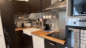 A modern kitchen with dark cabinets, a wooden countertop, a built-in dishwasher, a coffee maker, a kettle, and a microwave.