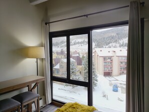 A room with a large window, a wooden desk, two chairs, and a yellow rug. - Copper Mtn. Studio Queen+Pull out ski in ski out (Copper Mountain)