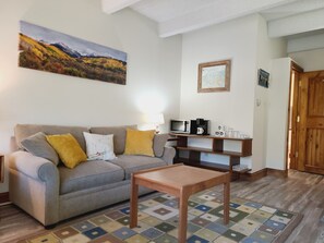 A living room with a sofa, a coffee table, a wall-mounted TV, a wooden cabinet, and a door. - Copper Mtn. Studio Queen+Pull out ski in ski out (Copper Mountain)
