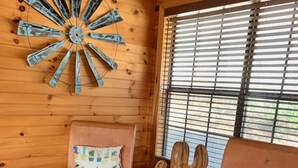 Two wooden chairs with red cushions and cactus-patterned pillows, a rustic wooden wall, and a window with blinds. - Rustic lodge retreat minutes from the Frio! (Concan)