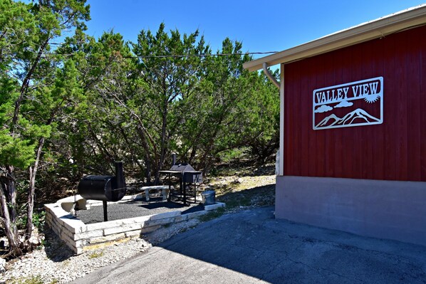 A red building with a sign reading "Valley View" and a barbecue area with a grill and seating. - Rustic lodge retreat minutes from the Frio! (Concan)