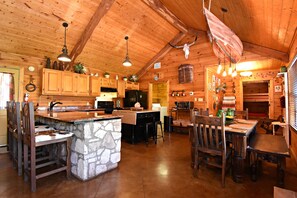 A rustic cabin-style kitchen with wooden cabinets, a stone island, and a dining area with wooden chairs. - Rustic lodge retreat minutes from the Frio! (Concan)