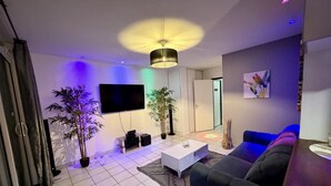 Una sala de estar moderna con un televisor de pantalla plana, un sofá negro, una mesa de centro y dos plantas en macetas.