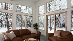 A spacious living room with large windows offering a snowy forest view.