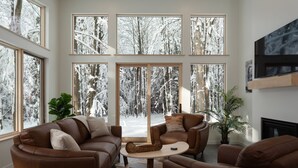 A cozy living room with large windows, leather sofas, a coffee table, and a fireplace.
