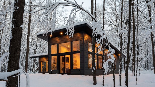 A wooden cabin with large windows, surrounded by snow-covered trees.