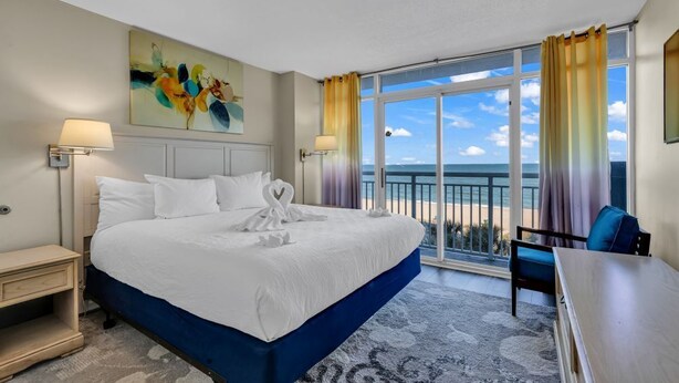 Habitación de hotel con una cama grande, un escritorio y vistas a la playa.