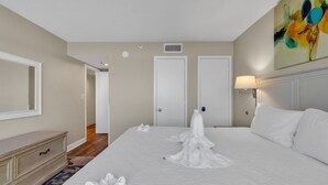 Una habitación de hotel con una cama grande, un aparador, un cuadro en la pared y una puerta.