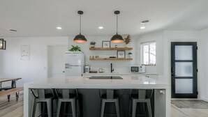 A modern kitchen with a large island, bar stools, pendant lighting, and built-in appliances.