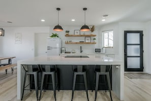 A modern kitchen with a large island, bar stools, pendant lighting, and built-in appliances.