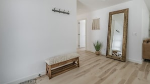A hallway with a wooden bench, a large mirror, and a potted plant.