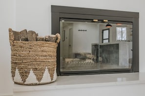 A woven basket with a white silhouette design on a white wall, next to a black-framed window with a mesh screen.