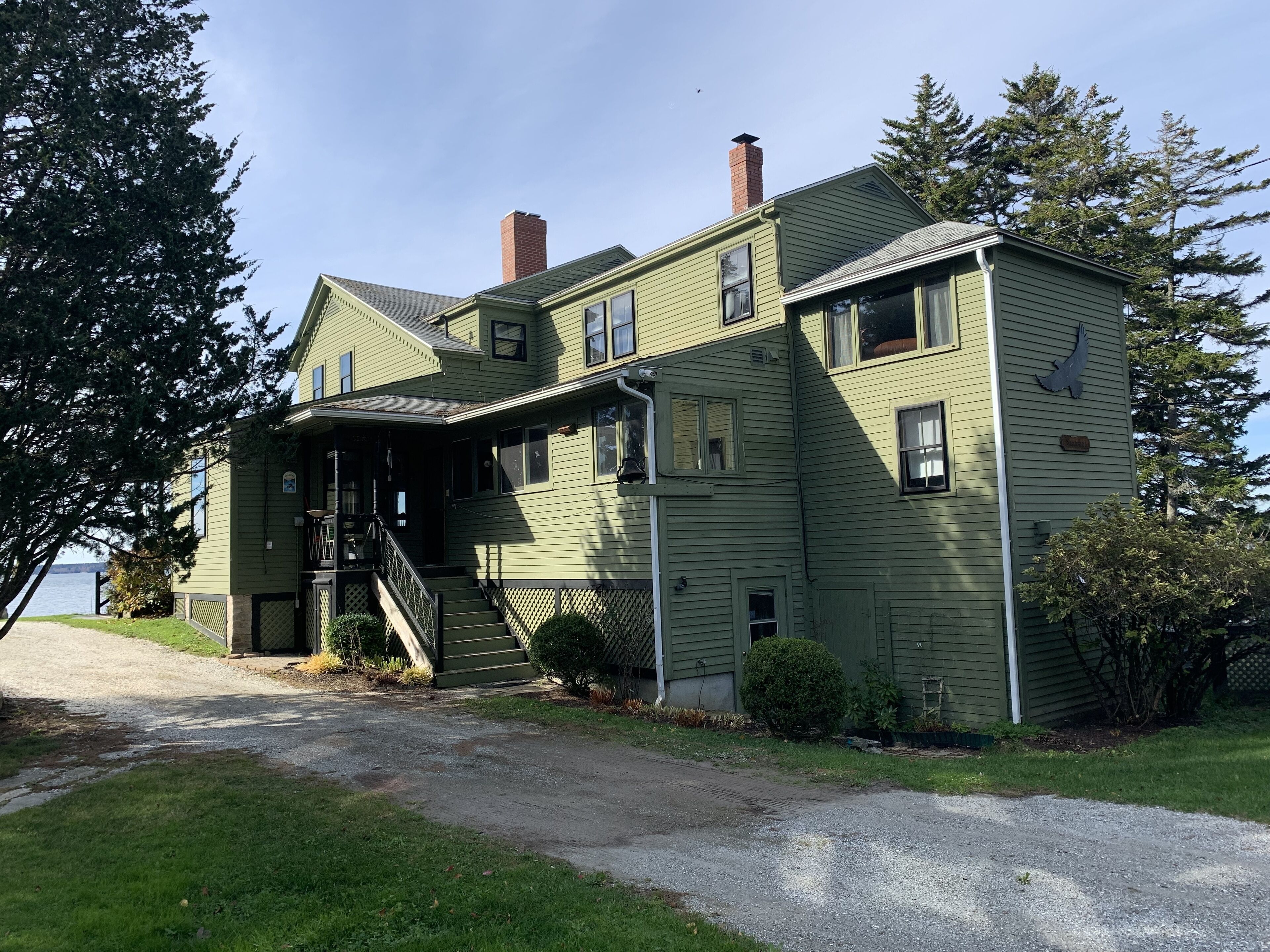 A two-story house with a porch, a chimney, and a view of the water.