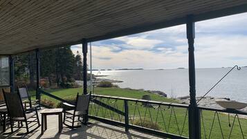Une terrasse couverte, aménagée avec du mobilier d’extérieur, qui offre une vue sur une étendue d’eau et une zone herbeuse.