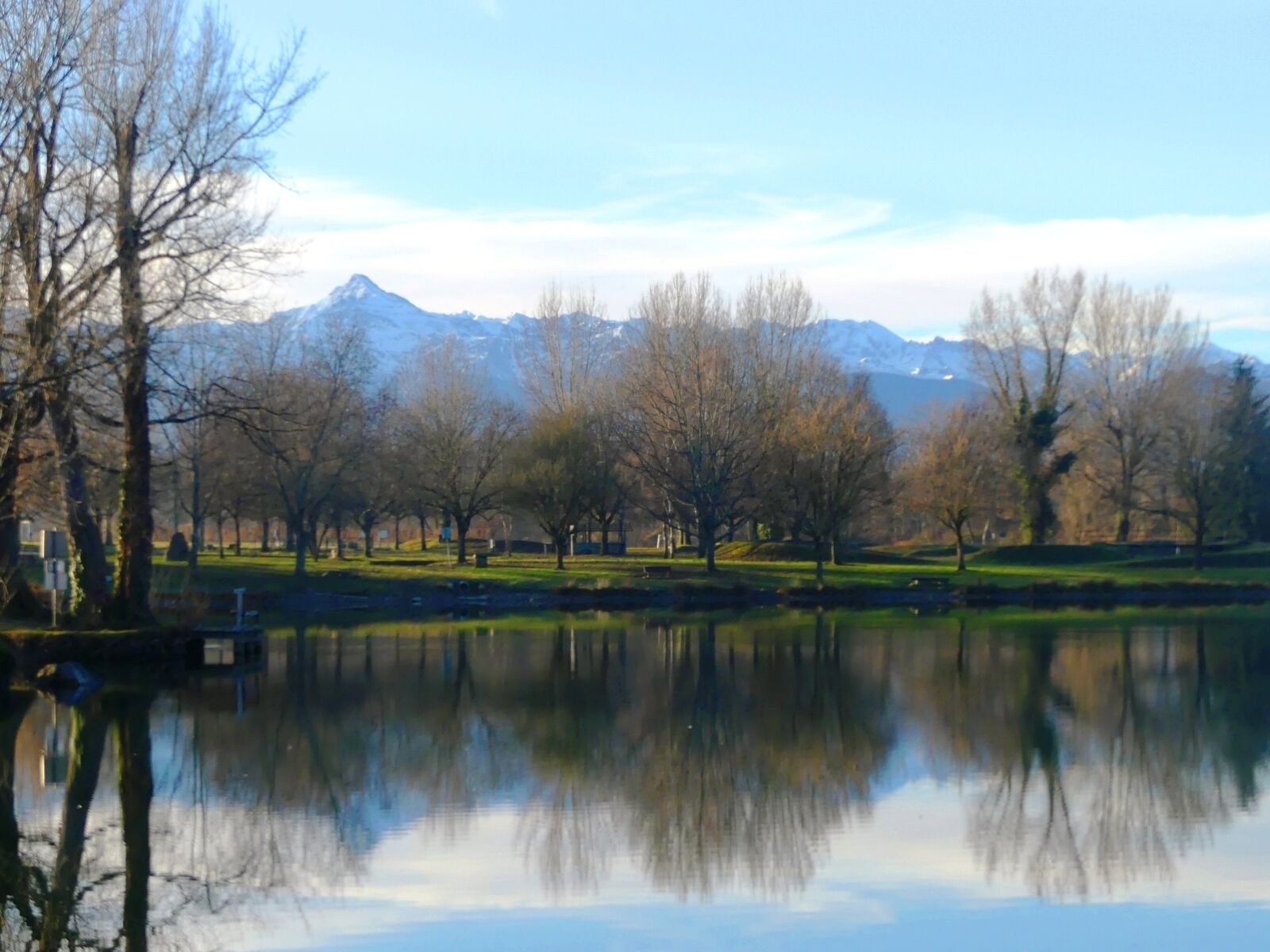 A park with a lake reflecting trees and mountains in the background.