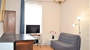 A small, well-lit room with a grey sofa, a television on a stand, a small white table with a vase, and a lamp. - APPALOOSA' (ministerial classification) quiet T2 apartment Tarbes near downtown  (Tarbes)