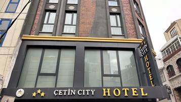 Um hotel com fachada moderna, grandes janelas e uma placa chamativa com a inscrição "Cetin City Hotel".
