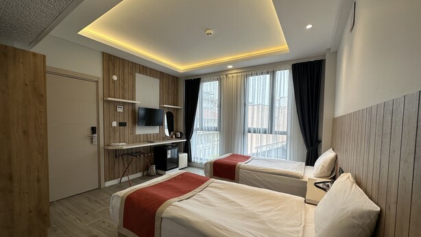 Una habitación de hotel moderna con dos camas, un televisor, un minibar y vistas a la ciudad.