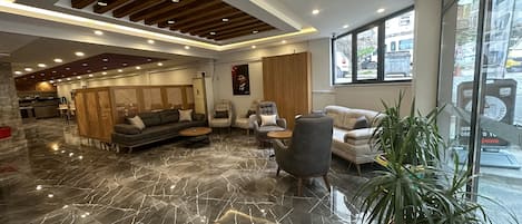 Una hall moderna di un hotel, con pavimento in marmo, zona salotto e ampie finestre.