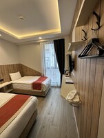 A hotel room with two beds, a desk, a mirror, and a window with curtains.
