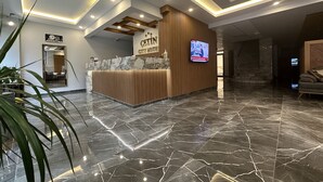 Zona de recepción de hotel con suelo de mármol, mostrador de madera y una pantalla de televisión.