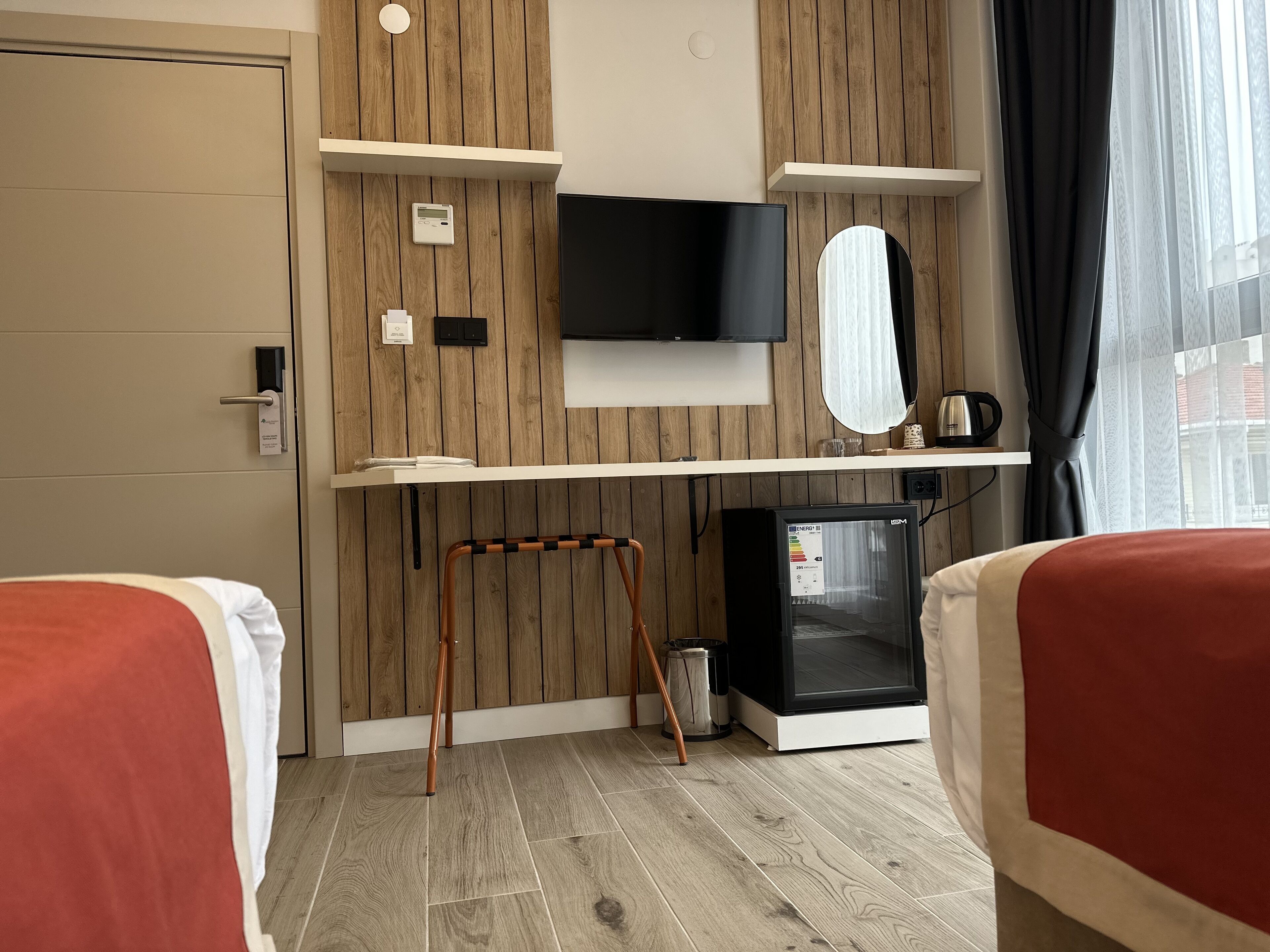 A hotel room with wooden panel walls, a flat-screen TV, a small refrigerator, a coffee maker, and two beds with red bedding.